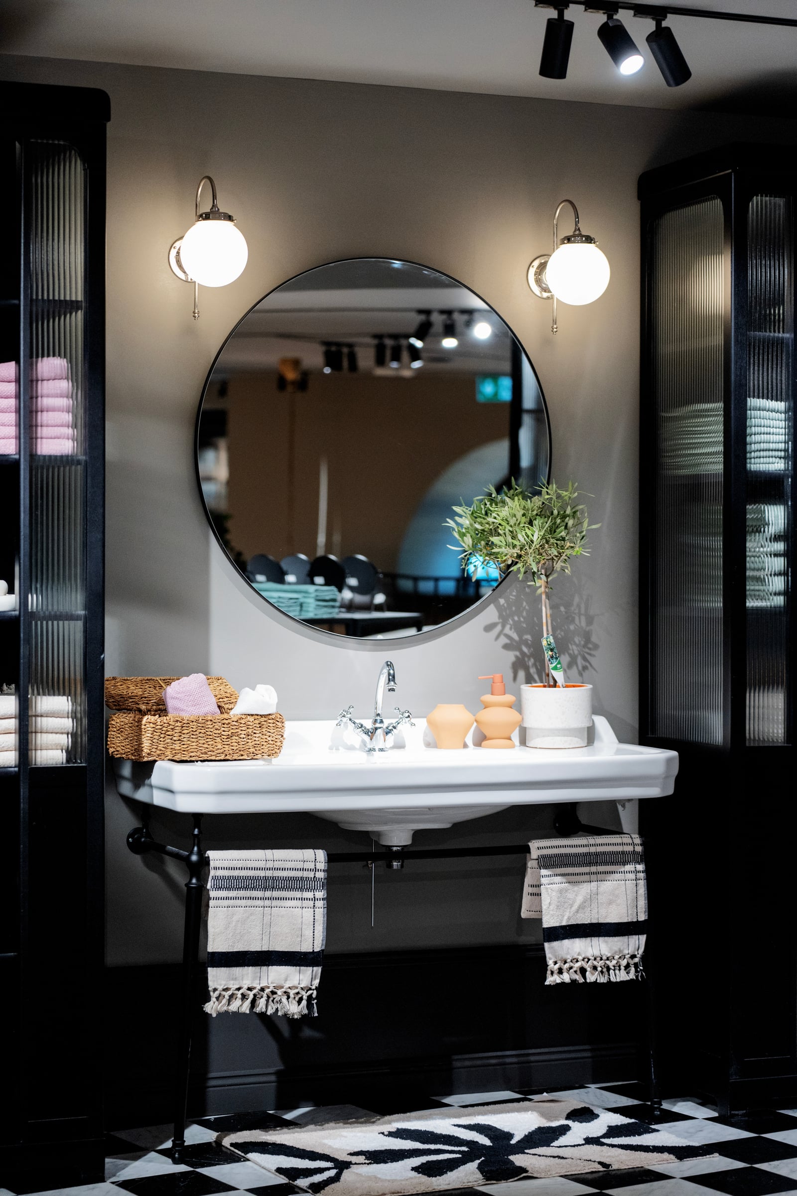 Lavabo, miroir rond et serviettes rayées dans l'espace salle de bain H&M Home