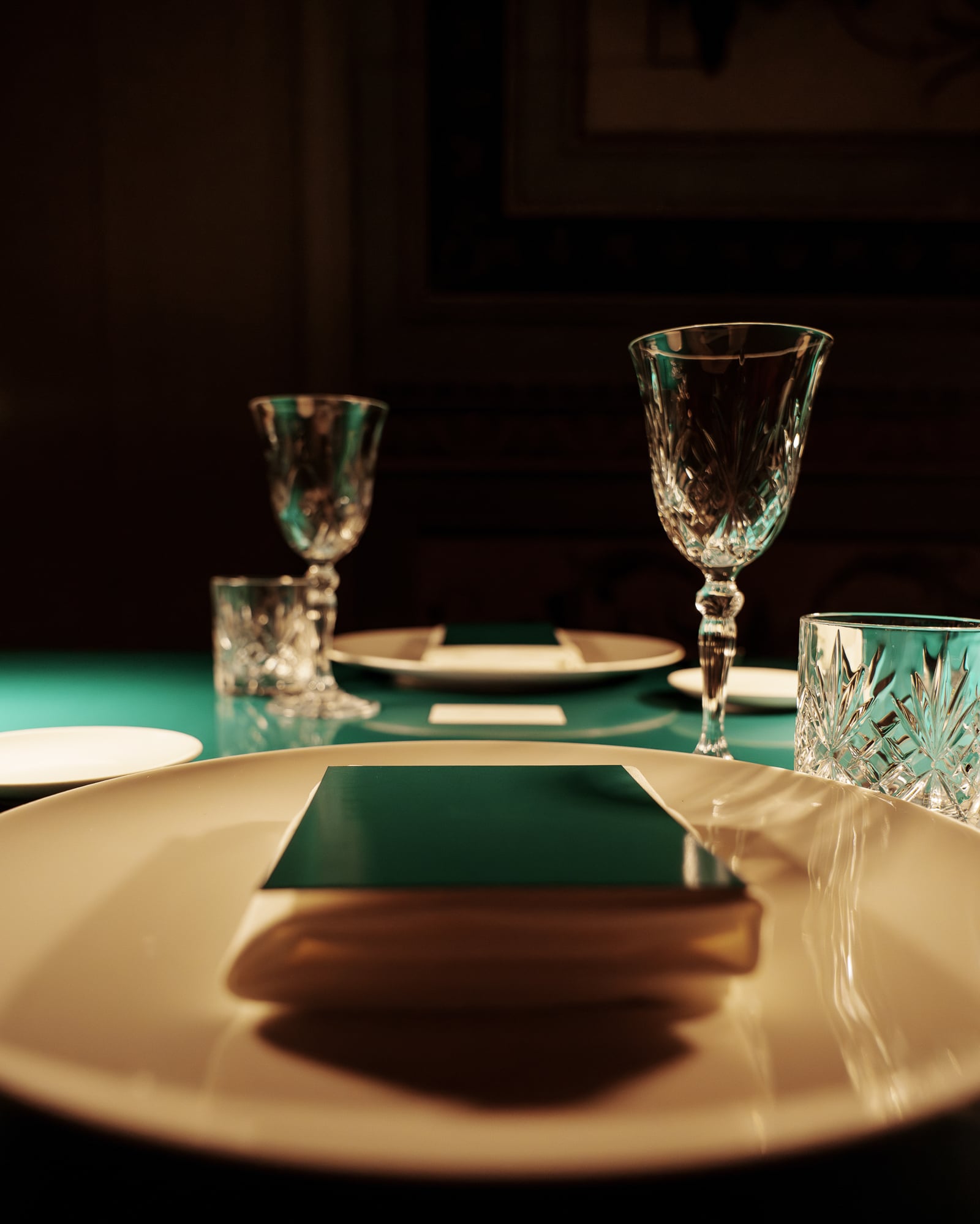 Assiette, carton vert et verres en cristal en lumière tamisée, dîner de gala à Palerme